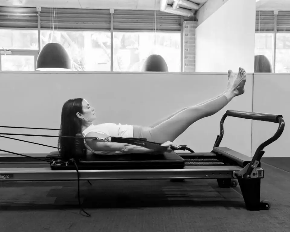 Woman lying supine on a Pilates reformer, with her legs extended upwards, performing an abdominal and leg exercise